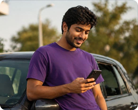 Smiling young man in purple shirt leans on car, viewing his smartphone.