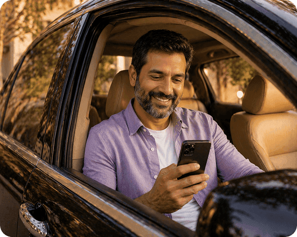 Smiling man with beard in a car, looking intently at his smartphone.