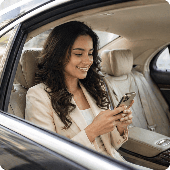 Smiling woman in a blazer uses her smartphone in the back seat of a luxury car.